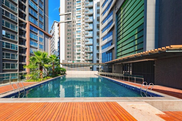Piscina com deck de madeira, cercada por edifícios altos com varandas.