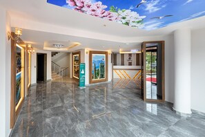 A hotel lobby with a marble floor, a reception desk, a staircase, and a wall with a floral mural. - Theluna Suite Hotel (Konyaalti)