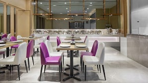Ein moderner Essbereich mit mehreren Tischen und Stühlen, einem Buffet und einem klaren, zeitgemäßen Design.