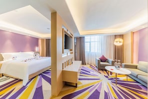 Quarto de hotel com cama, sofá, mesa de centro e televisão.