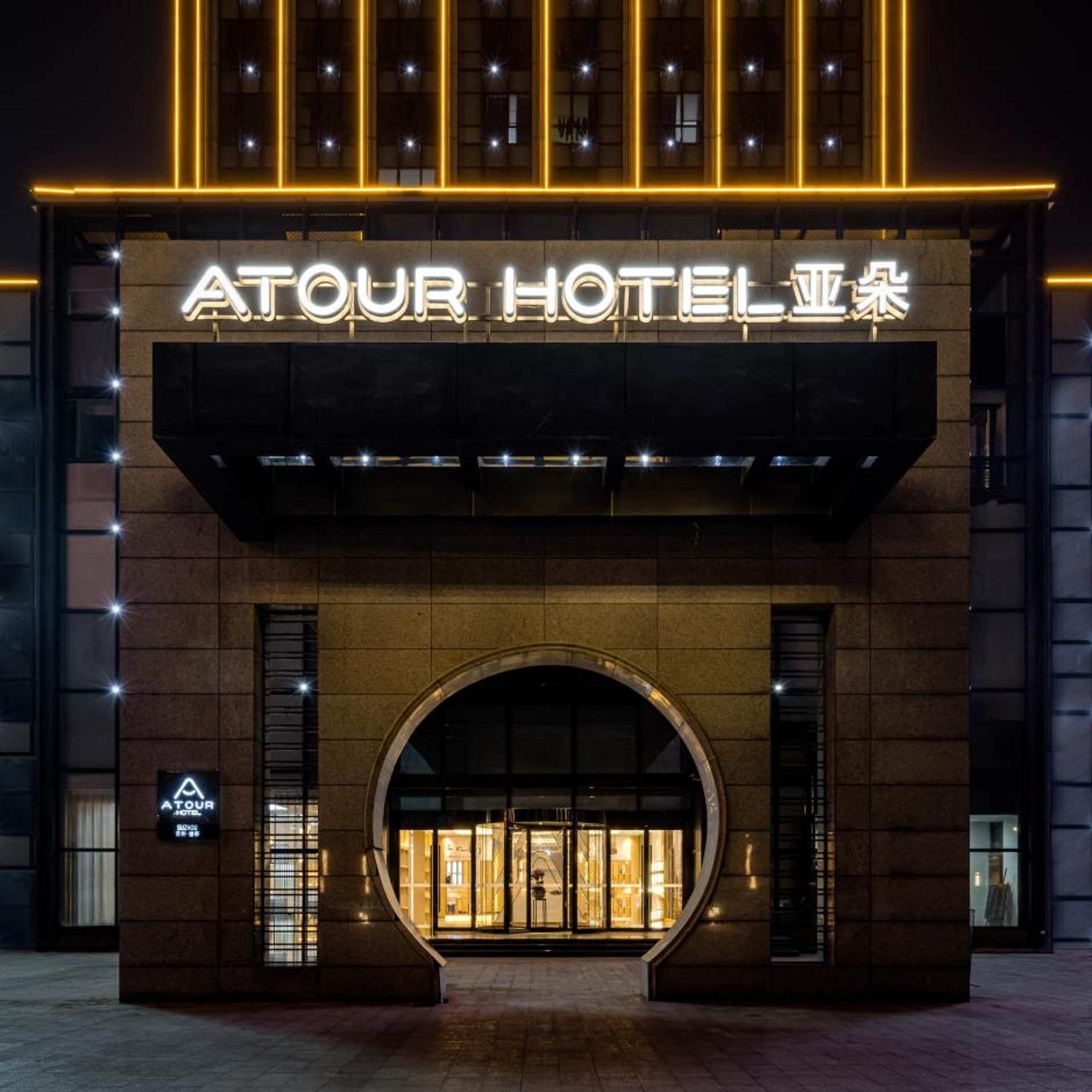 A hotel entrance with a large illuminated sign, a curved archway, and a well-lit facade.