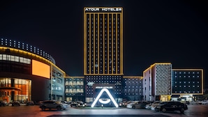 A hotel with a prominent vertical sign, multiple parking spaces, and a well-lit entrance. - Atour Hotel Wangting Suzhou (Suzhou)