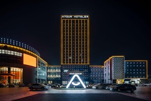 Um hotel com uma placa vertical chamativa, vários espaços de estacionamento e uma entrada bem iluminada.