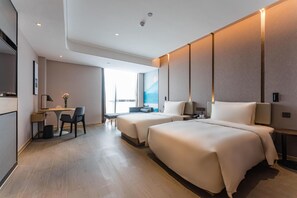 Quarto de hotel moderno com duas camas, uma escrivaninha e uma janela grande.