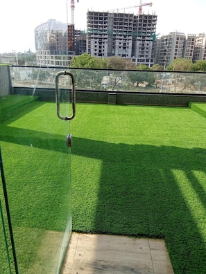 A rooftop with artificial grass, a glass door, and a view of a construction site in the background.