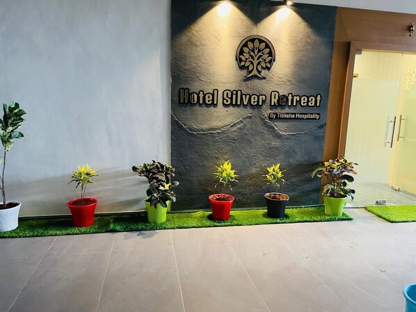 A reception area with a sign for Hotel Silver Retreat by Tiliksha Hospitality, potted plants, and a tiled floor.