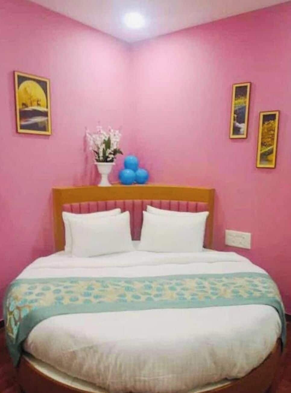 A bedroom with a bed, pink walls, and framed pictures.