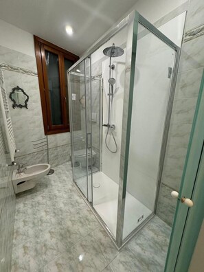 Ein modernes Badezimmer mit einer begehbaren Glasdusche, einem Standwaschbecken und einem Marmorboden.