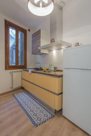 Eine kleine Küche mit eingebautem Herd, einem weißen Kühlschrank und einem Fenster mit Holzrahmen.