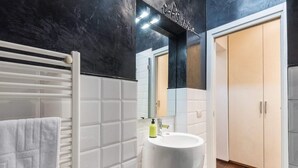 A bathroom with a white tiled wall, a white sink, a towel on a radiator, and a mirror above the sink. - Art Gallery Apartment in Florence (Florence)