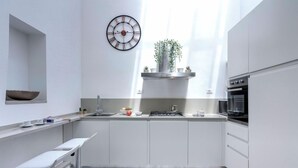 A modern kitchen with white cabinets, a stainless steel countertop, a built-in oven, and a wall-mounted clock. - Mamo Florence - Velluti Apartment (Florence)