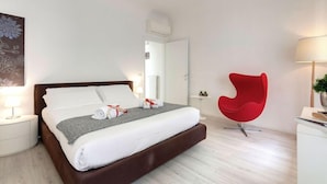 A modern hotel room with a large bed, a red chair, a bedside table, and a wall-mounted air conditioner. - Mamo Florence - Velluti Apartment (Florence)