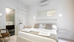A modern bedroom with a large bed, a built-in wardrobe, a vanity with a mirror, and an air conditioning unit. - Suite Jasmine (Florence)