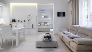 A modern living room with a sofa, a coffee table, and a TV mounted on the wall. - Suite Jasmine (Florence)