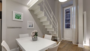 A dining area with a white table, chairs, a vase with flowers, a staircase, and a door with blinds. - Mamo Florence - St Elizabeth Loft Apartment (Florence)