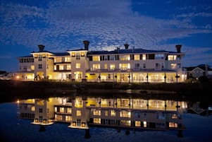 A multi-story waterfront property with balconies and a reflection in the water.