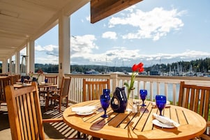 A covered outdoor dining area with tables and chairs, a wooden ceiling, and a view of boats and trees.