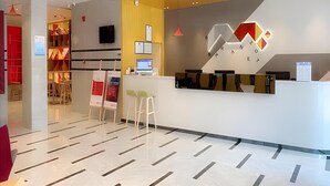 A hotel reception area with a modern design, including a reception desk, seating area, and a visible television screen. - Borrman Hotel (Huizhou)