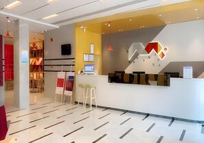 Un espace d’accueil d’hôtel au design moderne, comprenant un comptoir d’accueil, un coin salon et un écran de télévision bien visible.