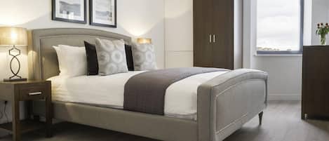 A bedroom with a bed, nightstand, dresser, wardrobe, and framed pictures on the wall.