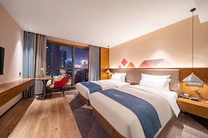 Quarto de hotel com vista para a cidade, duas camas, uma escrivaninha e uma cadeira.