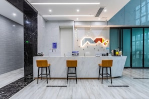Uma área de recepção moderna com balcão de mármore, três banquetas amarelas e uma instalação luminosa geométrica na parede.
