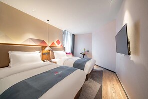 Quarto de hotel com duas camas, televisão, mesa de cabeceira e TV fixada na parede.