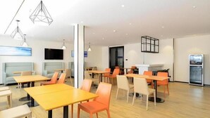 Et moderne spiseområde med borde, stole, et fladskærms-TV og et køleskab.