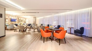 Een moderne hotellobby met een eetgedeelte met oranje stoelen, een flatscreen televisie en een bar.