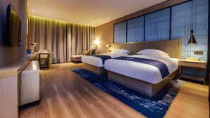 Een moderne hotelkamer met een groot bed, nachtkastjes, een bureau en uitzicht op de stad door de ramen.