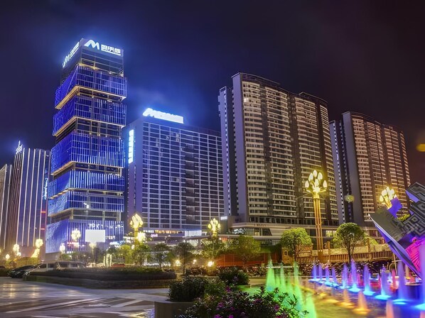 A nighttime cityscape with illuminated high-rise buildings, a water feature with fountains, and a well-lit public space. - Echarm Hotel (Qianxinan Buyei and Miao)