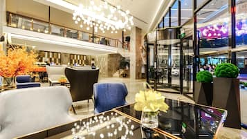 A modern hotel lobby with a reception desk, seating area, and a glass coffee table with decorative items.