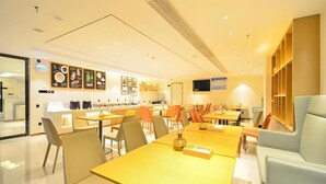 A modern dining area with multiple tables and chairs, a kitchen in the background, and a television mounted on the wall. - City Comfort Inn Enshi Jingang Baijia Plaza (Enshi)