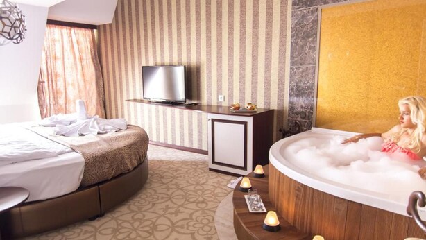 A hotel room with a bed, a television, a bathtub with candles, and a patterned carpet. - Izgrev Hotel (Struga)
