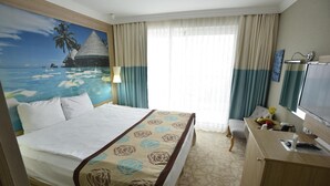 A hotel room with a bed, a desk, a television, and a painting of a tropical beach. - Izgrev Hotel (Struga)