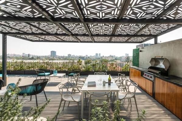 An outdoor patio with a view of a city skyline, featuring a grill and seating area. - Be Mate Condesa Hipodromo (Mexico City)