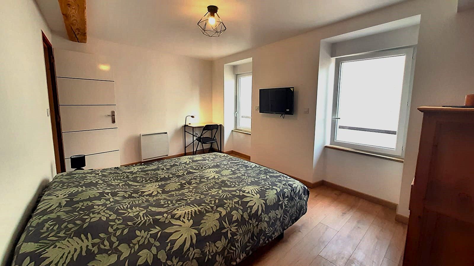 Un dormitorio con cama, escritorio, silla, televisor y ventana.