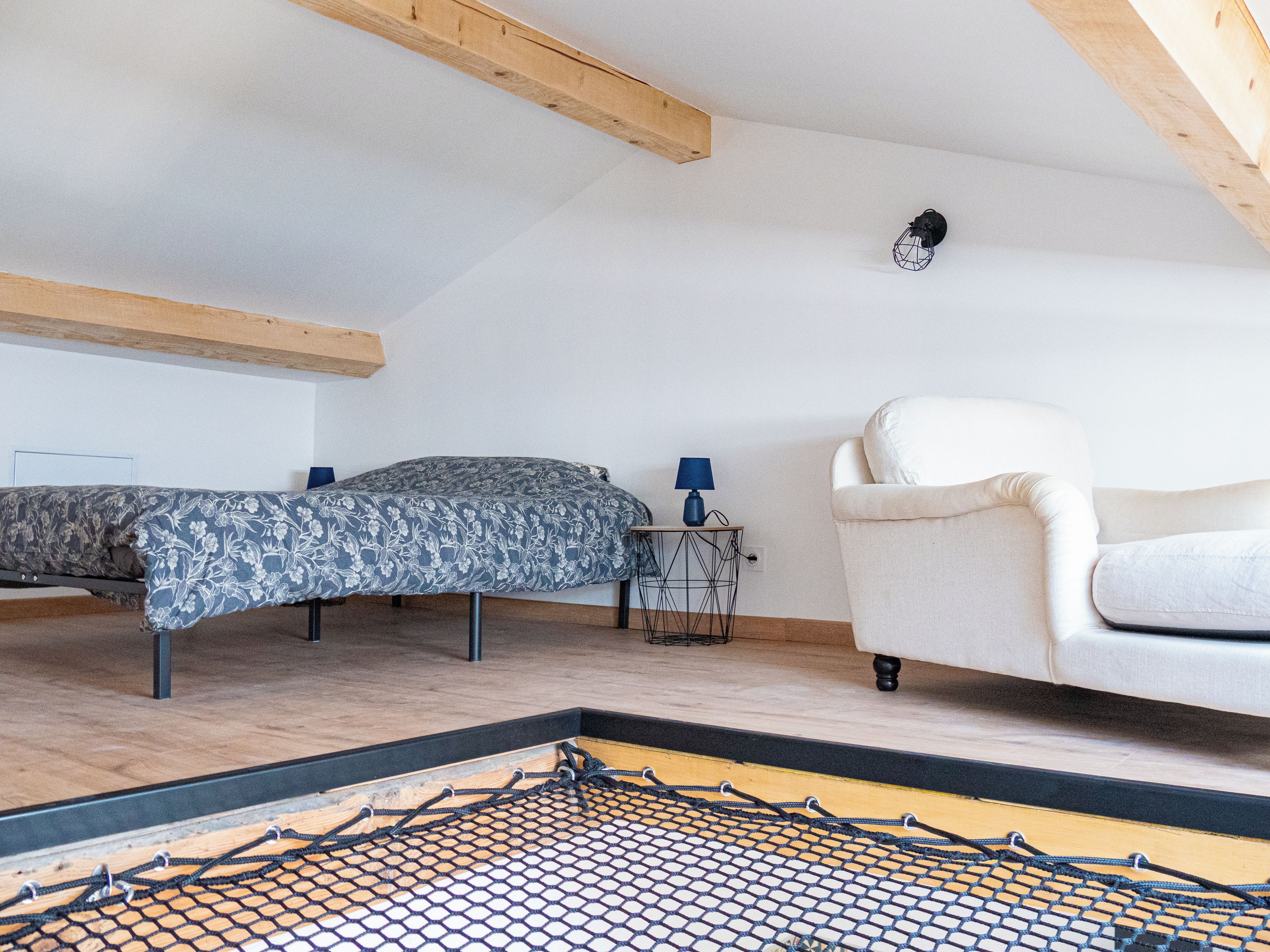 Una habitación con cama, una silla y una mesita de noche con lámpara.