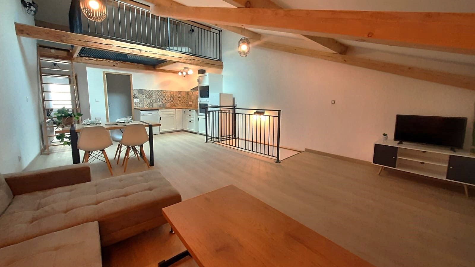 Un amplio salón con un conjunto de sofás, una mesa de comedor con sillas, una cocina al fondo y un televisor sobre un mueble.
