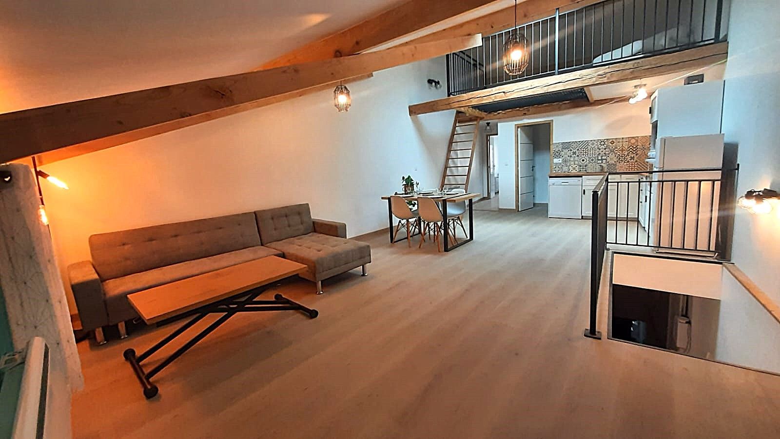 Un ambiente abitativo in stile loft con divano, tavolo da pranzo e sedie, una scala per un livello superiore e un angolo cottura.