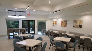 A spacious indoor dining area with multiple tables and chairs, large windows, and artwork on the walls. - Bonham Hotel (Bonham)
