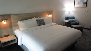 A hotel room with a large bed, bedside tables, a chair, and a wall-mounted lamp.