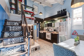 Une cuisine moderne dotée d’une cuisinière intégrée, d’un coin repas avec une table et d’un escalier orné de carreaux décoratifs.