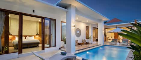 A modern hotel with a swimming pool, outdoor seating, and a well-lit interior.