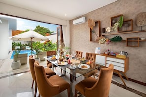 A dining area with a glass table, brown chairs, and a view of a swimming pool. - Monaco Blu Luxury Villas and Spa (Keroboken Kelod)