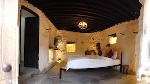 A bedroom with a bed, a chandelier, and stone walls. - Sama Wakan (Wakan)