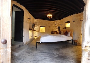 A bedroom with a bed, a chandelier, and stone walls. - Sama Wakan (Wakan)