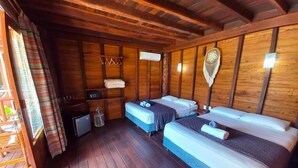Une chambre de style cabane avec des murs en bois, deux lits, une petite table et une fenêtre avec des rideaux.