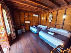 Una habitación estilo cabaña con paredes de madera, dos camas, una mesita y una ventana con cortinas.