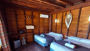 Une pièce de cabane en bois avec deux lits, un petit radiateur et un luminaire suspendu.